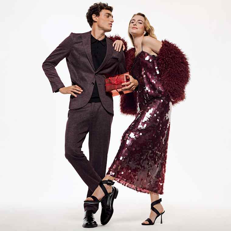 Woman wearing a festive red dress leaning on to a man in a brown suit